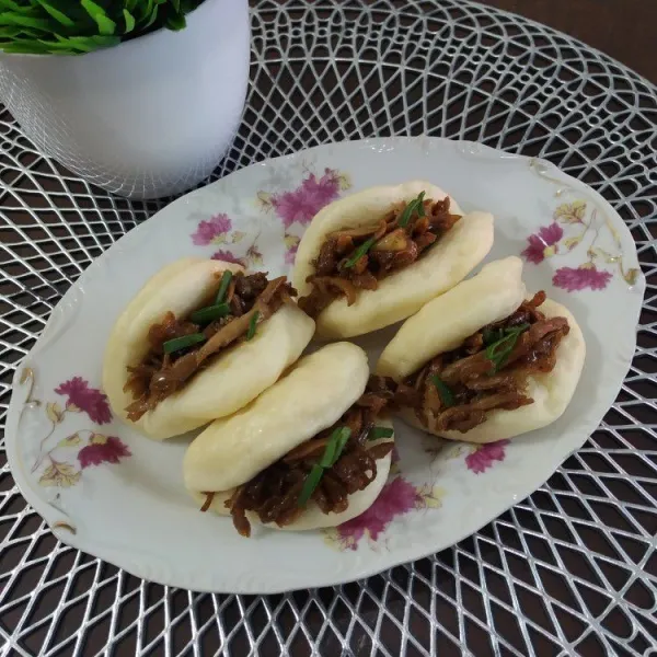 Ambil bakpao, selipkan isian ayam diantara celah lipatan, taburi daun bawang, sajikan hangat