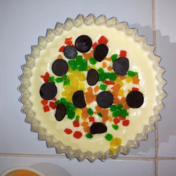 Masukkan whipping cream, aduk rata. Tuang adonan di atas loyang. Beri taburan bahan isian. Simpan di lemari es 30 menit.