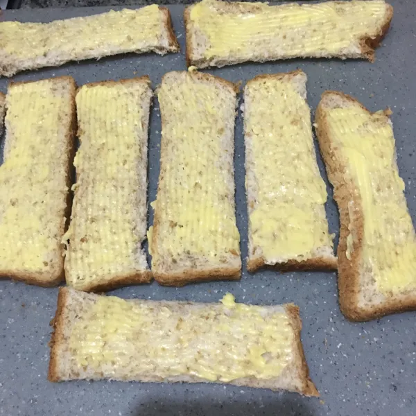 Semir dengan margarin pada permukaan roti tawar.