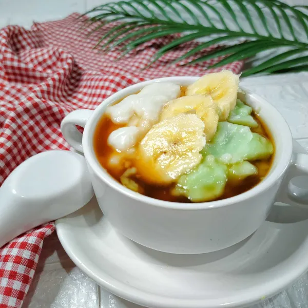 Tata di mangkuk saji bubur hijau dan putih siram dengan kuah gula rasa pisang.