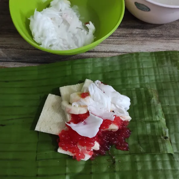 Pertama, letakkan daun pandan pada daun pisang. Kemudian tambahkan sagu mutiara, kelapa muda dan pisang.