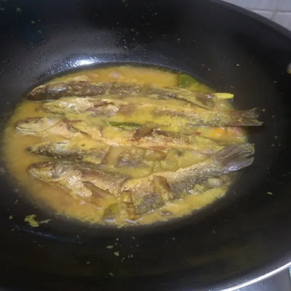 Masukkan ikan goreng, bolak balik sekali saja, diamkan sampai air agak surut/ sampai bumbu meresap ke dalam ikan.