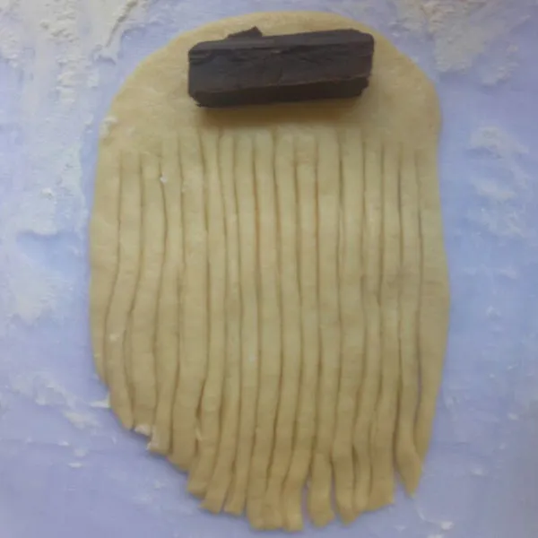 Taburi tipis tepung dialasnya, lalu gilas adonan dengan menggunakan rolling pan lalu potong memanjang jangan sampai putus, beri coklat batang di atasnya. Gulung adonan hingga rapi