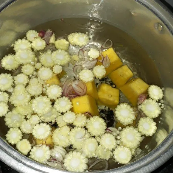 Rebus air hingga mendidih, masukkan labu, jagung putren, bawang merah, dan bawang putih.