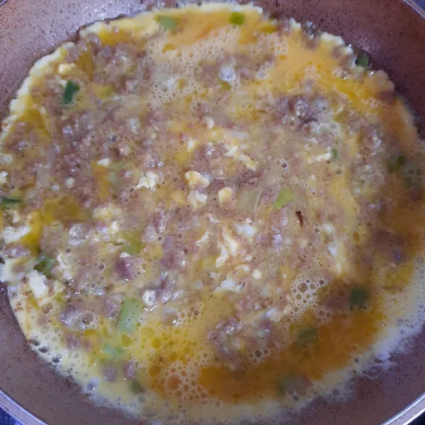 Tuang telur yang sudah dikocok lepas. Masak hingga bagian bawahnya cukup kokoh dan berkulit.