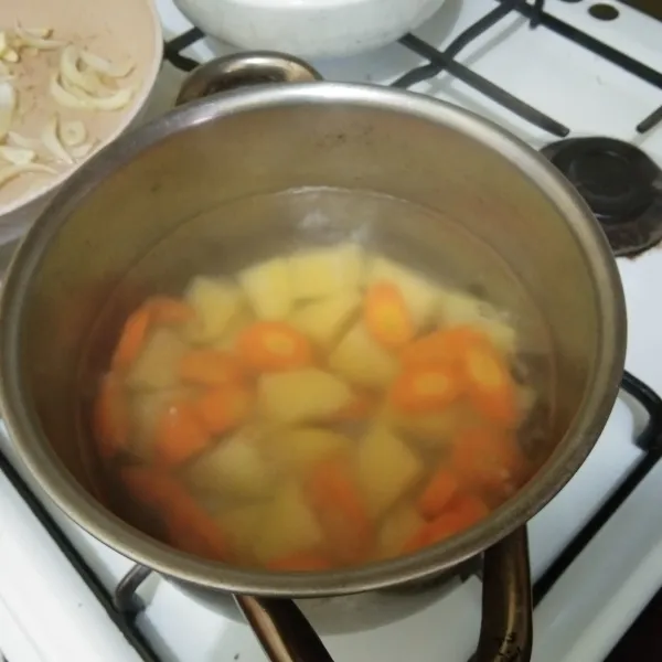 didihkan air dalam panci, masukan potongan kentang dan wortel, masak hingga setengah matang.