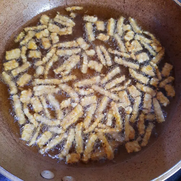 Goreng tempe hingga garing, angkat. Tips: agar tempe cepat garing, goreng tempe sedikit-sedikit dalam minyak banyak dan panas.