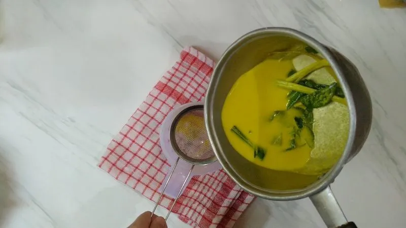 Membuat santan, masukan santan ke dalam panci lalu masukan kunyit yang sudah diambil sarinya, daun pandan, daun jeruk dan sereh. Kemudian panaskan hingga mendidih lalu disaring