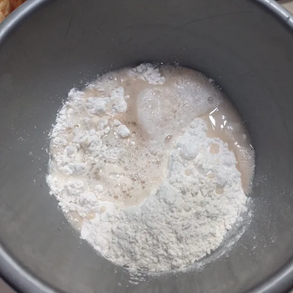 Masukan tepung ke dalam wadah, lalu masukkan biang dan sisa air sedikit demi sedikit, uleni sampai tercampur rata