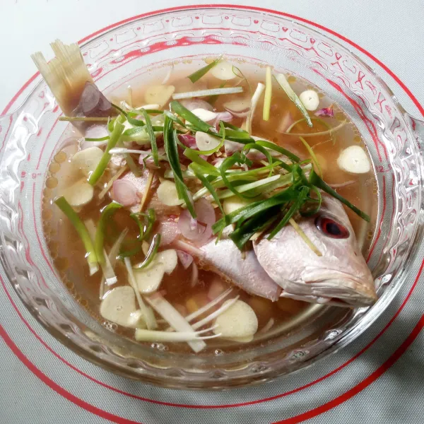 Taburkan jahe, bawang merah, bawang putih dan daun bawang di atas ikan.