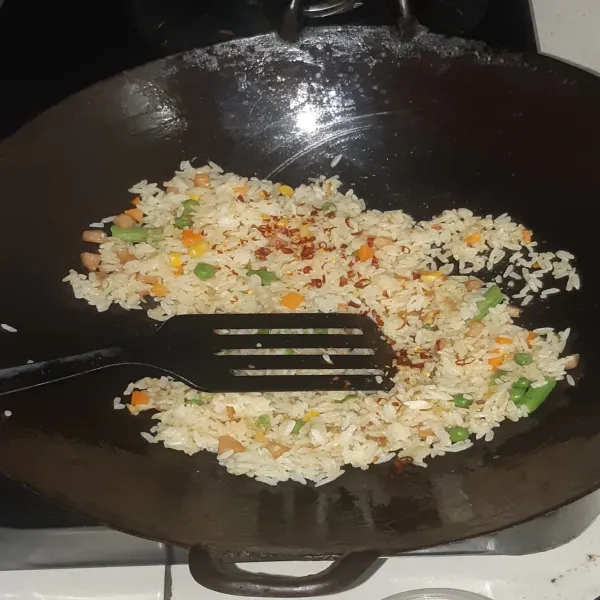 Masukkan nasi, tambahkan bumbu dan chili flakes, lalu aduk rata.