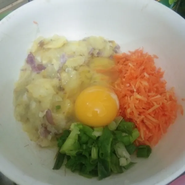 Tuang kentang pada mangkuk, tambahkan telur, garam, kaldu jamur, irisan bawang daun dan wortel parut, aduk rata