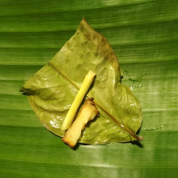 Ambil dua lembar daun pisang yang sudah di lap bersih kemudian beri potongan daun salam, potongan serai dan lengkuas.