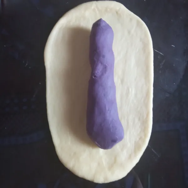 Ambil 1 bagian dough lalu pipihkan memanjang menggunakan rolling pin. Letakkan 1 isian ubi ungu, kemudian lipat atau bungkus isian ubi ungu dengan dough.