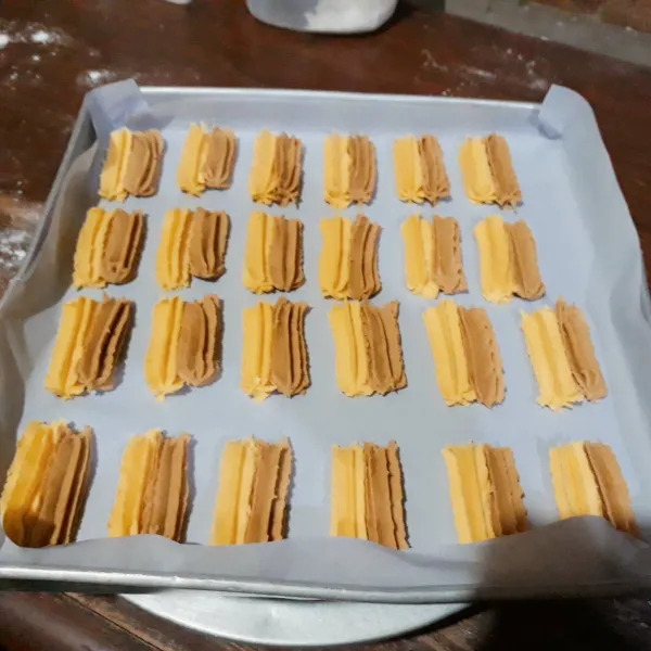 Masukkan adonan dalam plastik segitiga. Alasi loyang dengan kertas roti. Semprit adonan kuning & mocca memanjang.