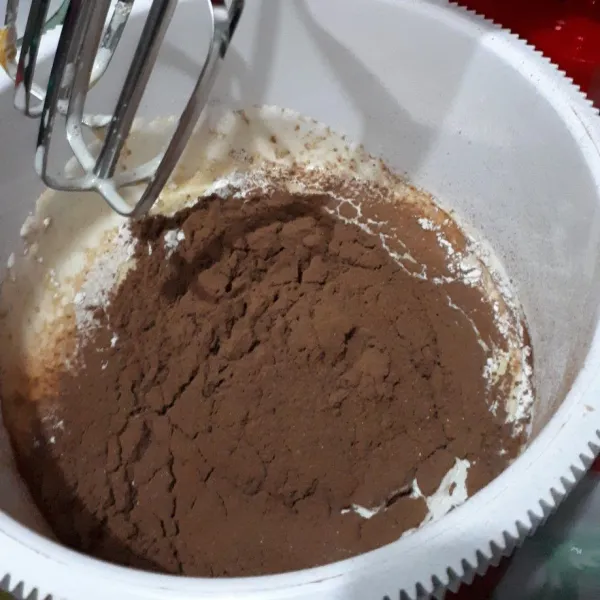 Setelah tercampur rata, masukkan tepung terigu dan coklat bubuk yang telah diayak, mixer sebentar hingga tercampur asal. Kemudian masukkan lelehan coklat tadi, mixer selama semenit hingga menyatu, jangan terlalu lama.