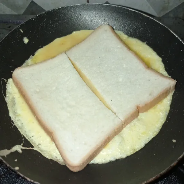 Panaskan teflon dengan 1 sdt margarin, lalu tuang kocokan telur tata roti tawar diatas telur masak sampai bagian bawah matang.
