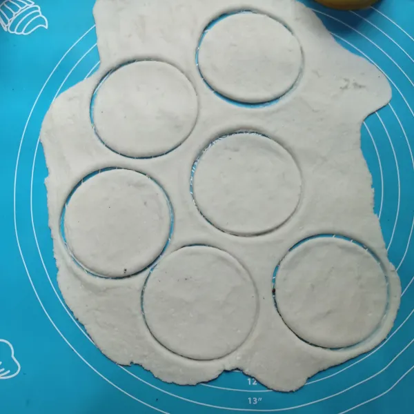 Baluri meja kerja dengan tepung tapioka lalu gilas adonan dengan rolling pin, cetak dengan mangkuk kecil, lakukan sampai selesai