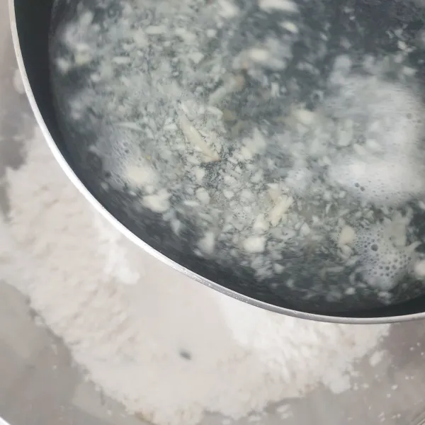 Tuangkan air rebusan bawang putih ke dalam campuran tepung, aduk rata dengan menggunakan spatula.