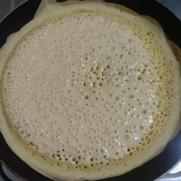 Aduk cepat lalu tuangkan pada teflon panas, buat pinggiran kulit dengan bantuan sendok sayur. Tunggu sampai muncul gelembung yang banyak di atas adonan.