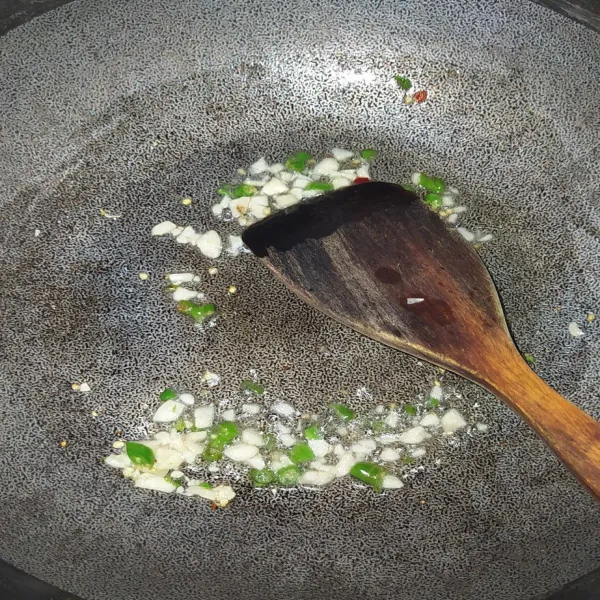 Tumis bawang putih cincang hingga harum, lalu tambahkan potongan cabai rawit. Tumis hingga cabai rawit layu.