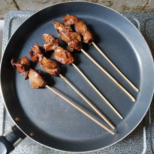 Tusuk ati ayam dengan tusukan sate, panggang di atas teflon hingga kecoklatan.