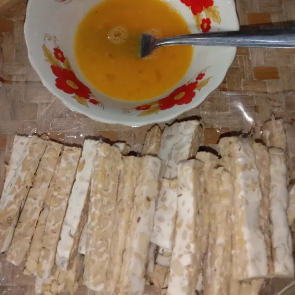 Potong tempe seperti stik kira-kira sebesar jari telunjuk dan kocok telur yang sudah dicampur dengan garam dan merica