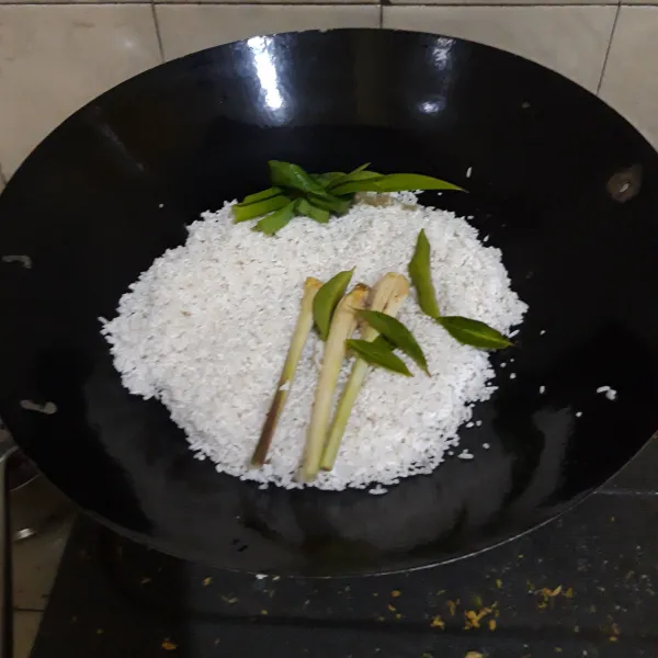 Siapkan wajan. Masukkan beras, serai, daun salam, dan daun pandan.