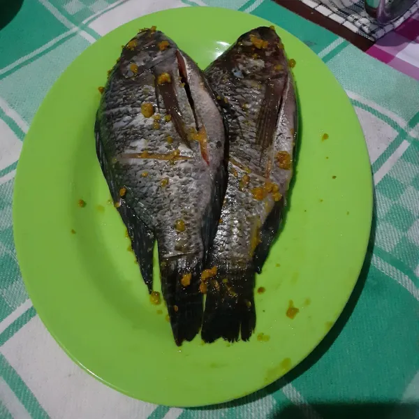 Bersihkan ikan mujair. Haluskan bawang putih, kunyit, dan garam. Kemudian lumurkan keseluruh ikan mujair bersama perasan jeruk nipis. Marinasi selama kurang lebih 20 menit.