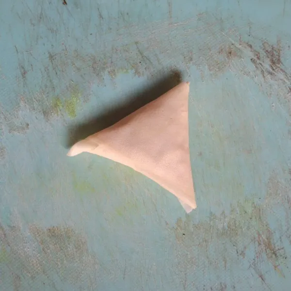 Lipat secara berulang mengikuti sudut segitiga, pada ujung kulit lumpia rekatkan dengan larutan terigu.
