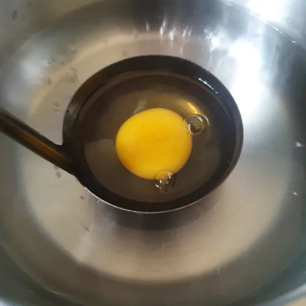 Kurangin apinya, masukkan telur yang sudah dipecahkan dalam centong sayur (ladle). Usahakan jangan sampai terendam.