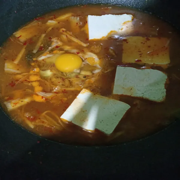 Potong tahu menjadi 2 bagian lalu masukkan dalam kuah. Masukkan juga telur, masak hingga telur setengah matang atau sesuai selera. Sajikan dengan irisan daun bawang diatasnya.