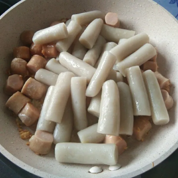 Setelah sosis setengah matang, masukkan potongan kue beras kemudian aduk rata.