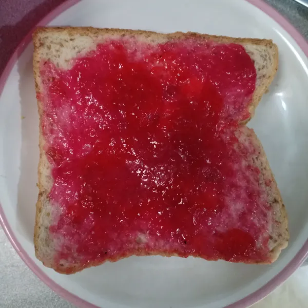 Tutup dengan 1 lembar roti dan oles dengan selai strawberry