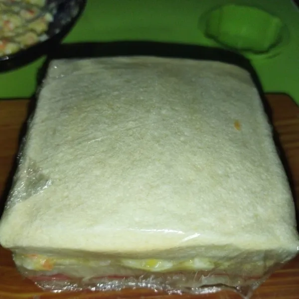 Tutup dengan 1 lembar roti, lalu bungkus dengan plastik wrap, agar sandwich tidak berantakan saat dipotong.