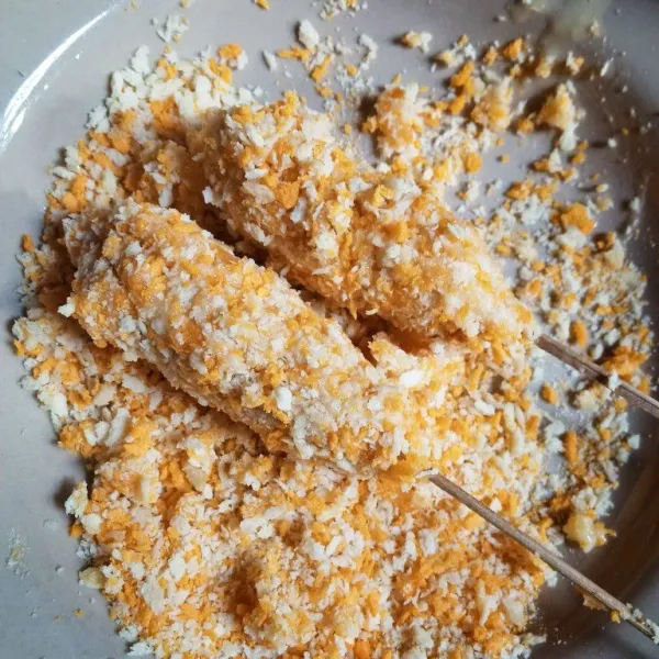 Setelah dimasukkan ke adonan, angkat Corndog dan lumuri dengan tepung panir dengan menekan agar lapisan Corndog padat sempurna.
