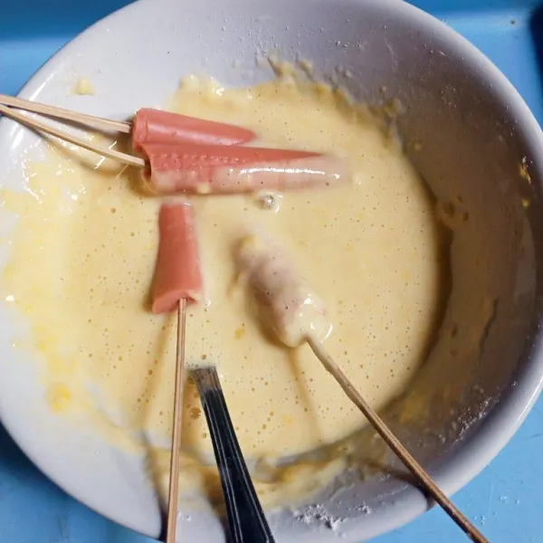 Potong sosis jadi dua ,lalu tusuk dengan tusukkan sate kemudian celupkan ke dalam adonan.