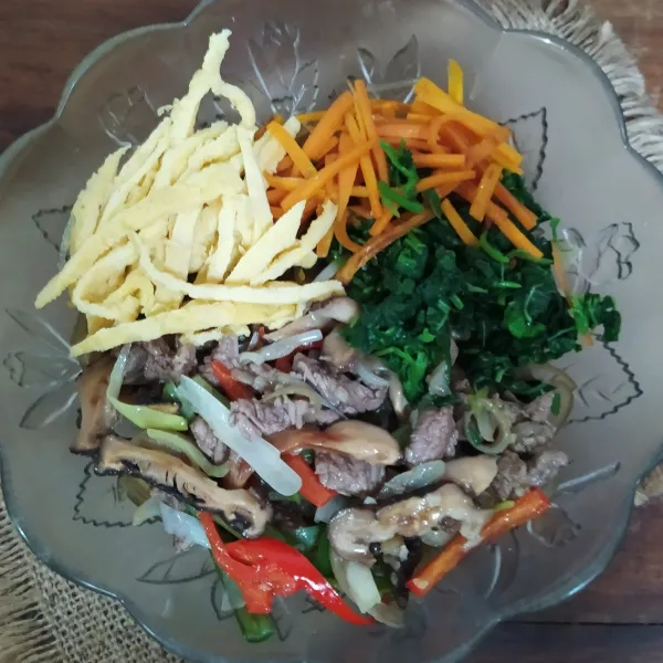 Masukkan tumisan daging dan jamur ke mangkuk berisi bihun/dangmyeon. Masukkan juga wortel, bayam, telur, dan wijen sangrai. Aduk rata menggunakan tangan yang dibungkus sarung tangan plastik sambil dicicipi. Jika masih ada yang kurang pas, bisa ditambahkan bumbunya sesuai selera.