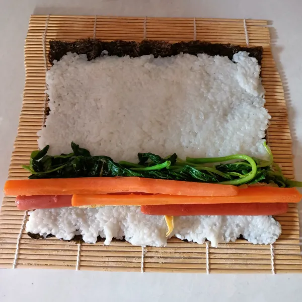 Siapkan susi roll, letakkan 1 lembar nori diatasnya, kemudian nasi diratakan keseluruh permukaan nori. Beri isian berupa sayuran, telur, sosis, kemudian gulung perlahan sambil ditekan untuk memadatkan agar tidak mudah rontok.