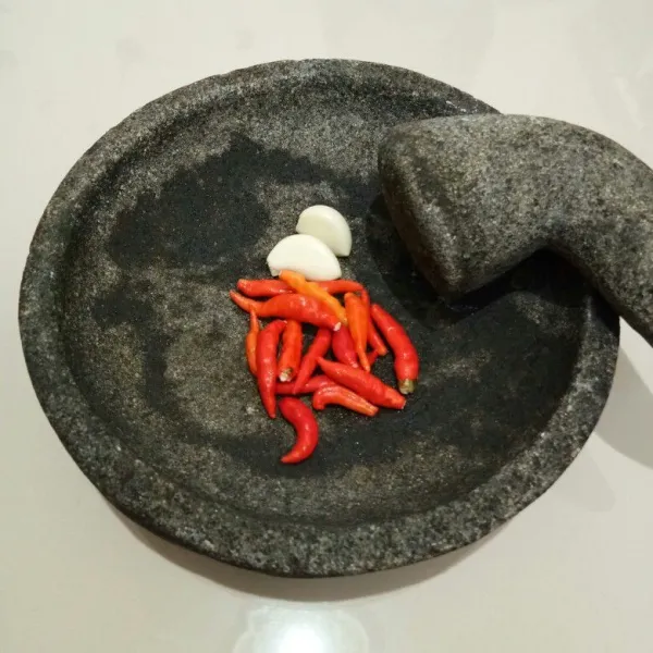 Masukkan cabe rawit dan bawang putih ke dalam cobek. Lalu uleg kasar saja.