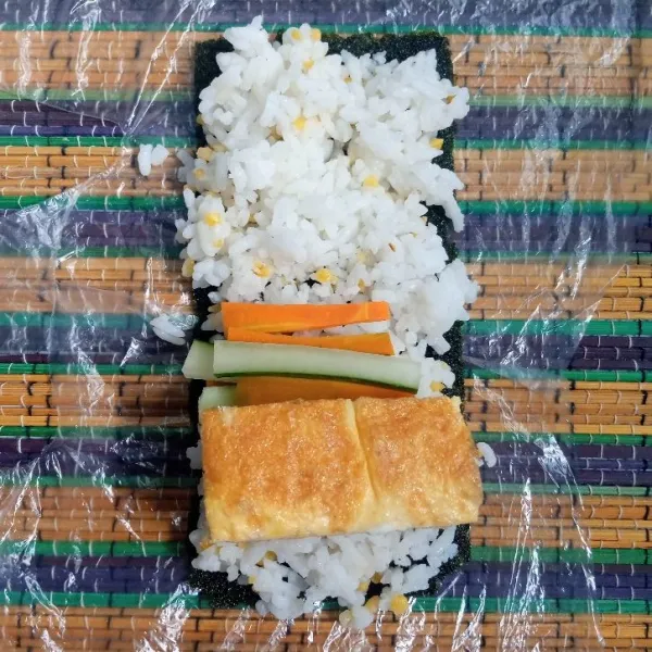 Siapkan nori. Tambahkan nasi, telur gulung,timun dan wortel diatasnya. Kemudian gulung.