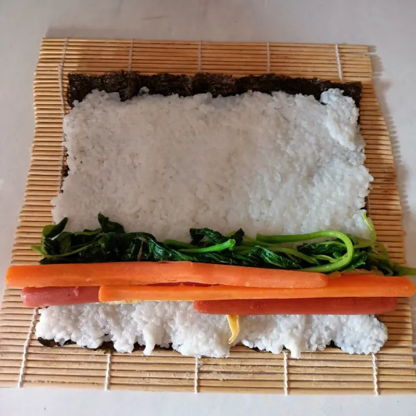 Siapkan 1 lembar nori. Beri nasi dan ratakan, letakkan semua bahan isian.