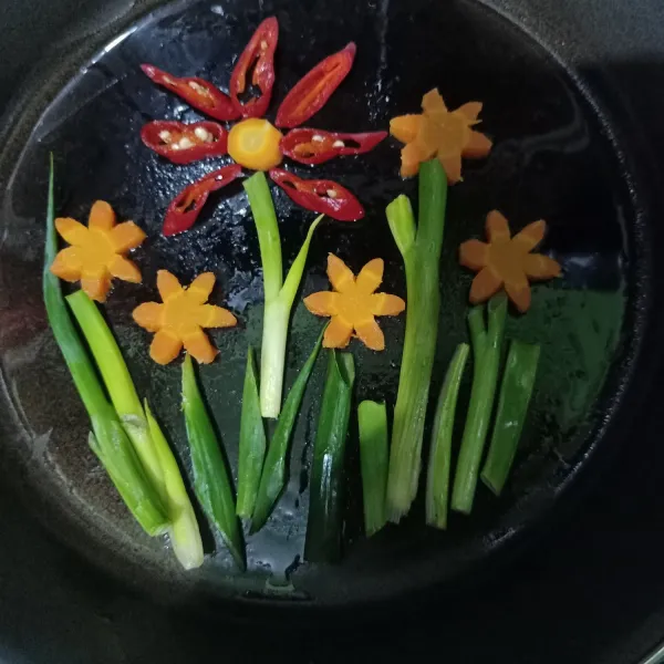 Siapkan wajan lalu olesi minyak goreng. Tata sayuran di dalam wajan berbentuk bunga dari sayuran yang telah dipotong sebelumnya. Tata irisan cabe merah menjadi bunga.