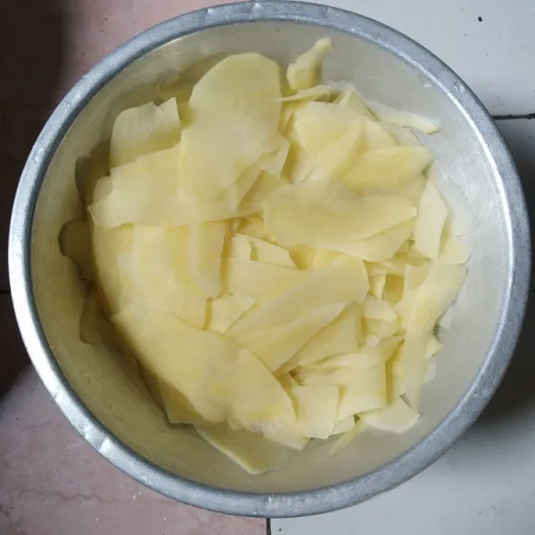 Kupas kentang dan iris tipis menggunakan peeler.