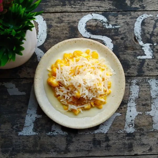 Sajikan cheesy sweet corn selagi hangat, tambahkan topping keju parut diatasnya.