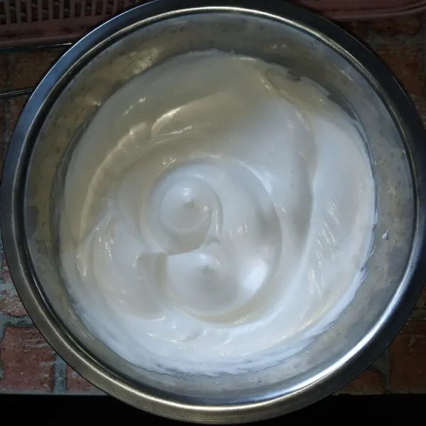 Buat meringue (kue busa) dengan mixer putih telur dan gula pasir hingga stiff peak (adonan putih mengembang kaku dan belum sampai air).