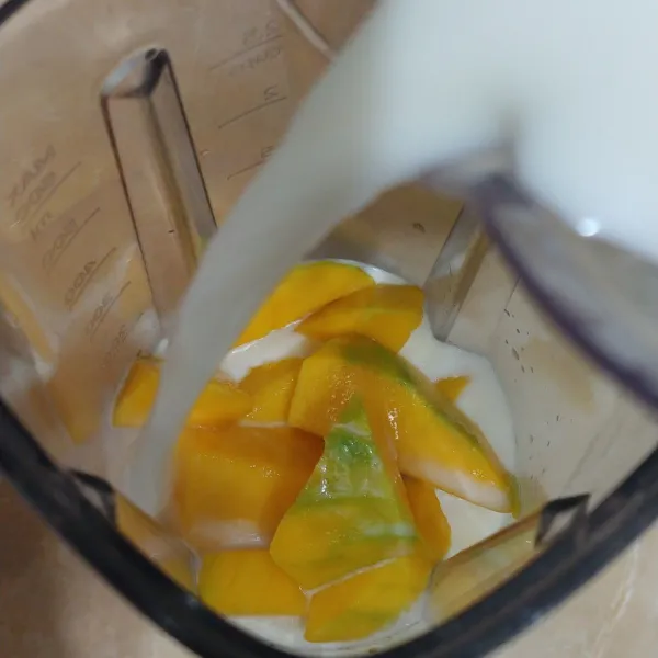 Tuang buah mangga yang sudah dikupas ke dalam gelas blender. Tambahkan susu cair.
