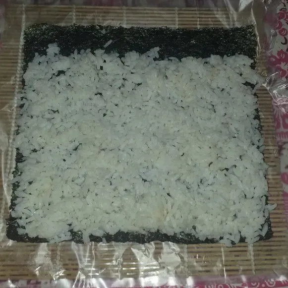 Siapkan sushi mate yang telah dilapisi plastik agar tidak lengket. letakkan nori kemudian nasi, ratakan ke setiap sisi. Sisakan sedikit bagian.