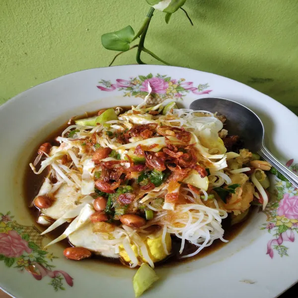 Penyajian tata dalam piring irisan ketupat, tahu, mie bihun, kol, daun seledri, cabe rawit. Siram kuah taburi bawang goreng dan kacang goreng.