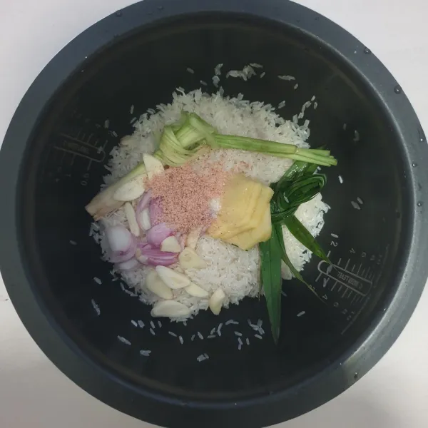 Siapkan panci rice cooker. Masukkan beras yang telah dicuci bersih lalu masukkan garam, gula pasir, kaldu jamur, bawang merah, bawang putih, pandan, serai, dan jahe.